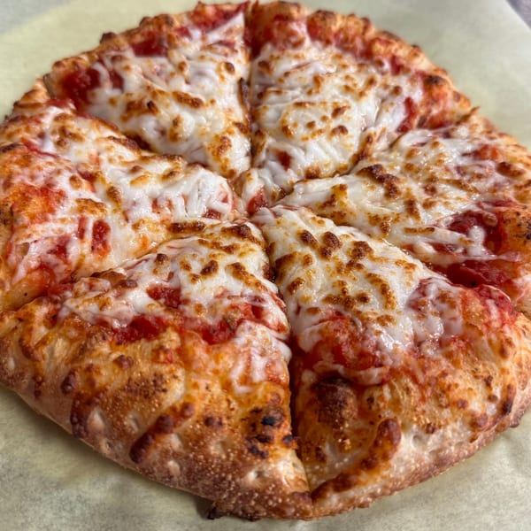 A freshly baked Amelio's Pizza and More cheese pizza, sliced into eight pieces, on parchment paper.
