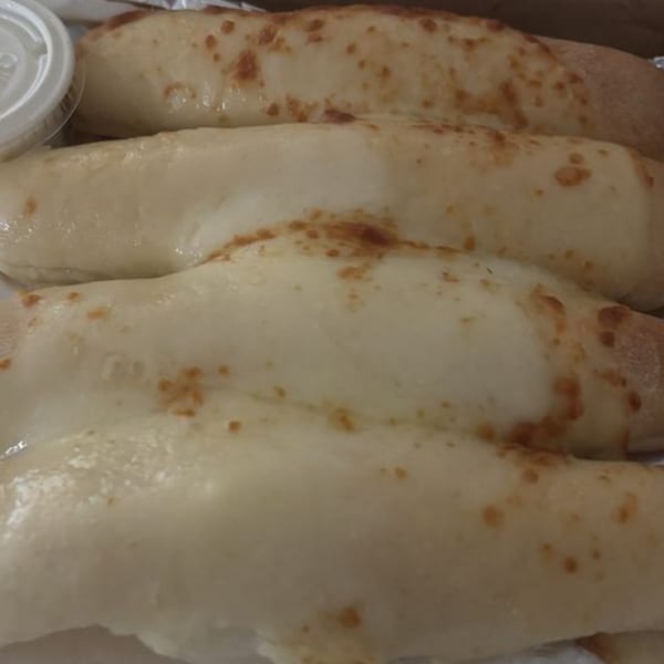 Four golden-brown Amelio's Pizza and More breadsticks with melted cheese, served with a side of dipping sauce.